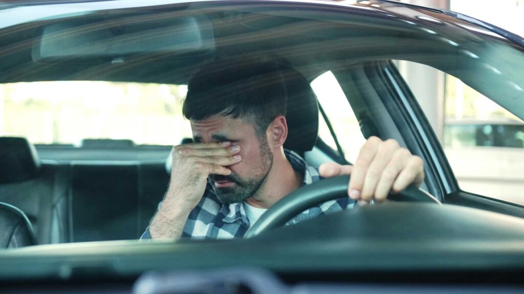 Un homme dans sa voiture qui se frotte les yeux de fatigue